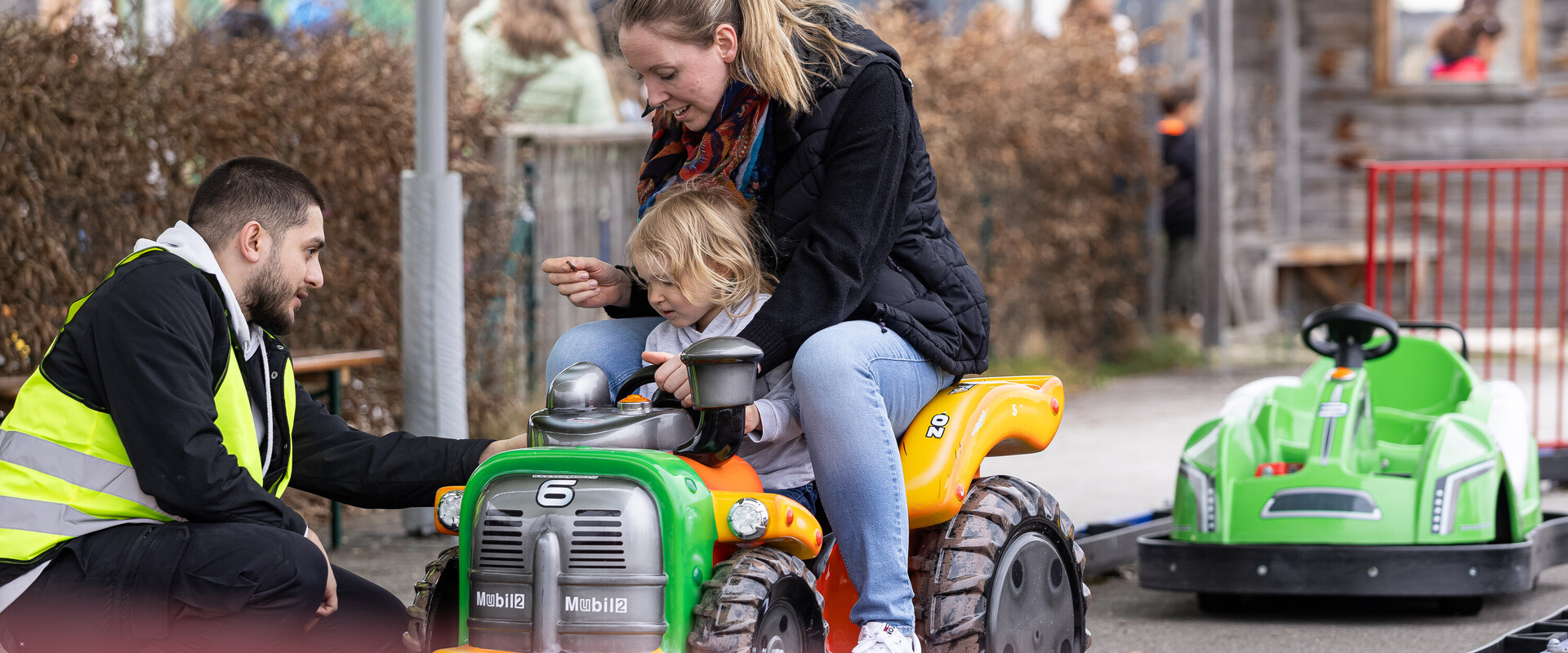 Mutter mit Kind sitzt auf E-Kart und wird von KLIMA ARENA Mitarbeiter eingewiesen.